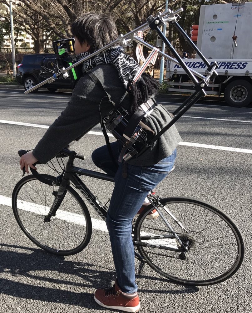 撮影機材を背負って自転車で撮影する山﨑